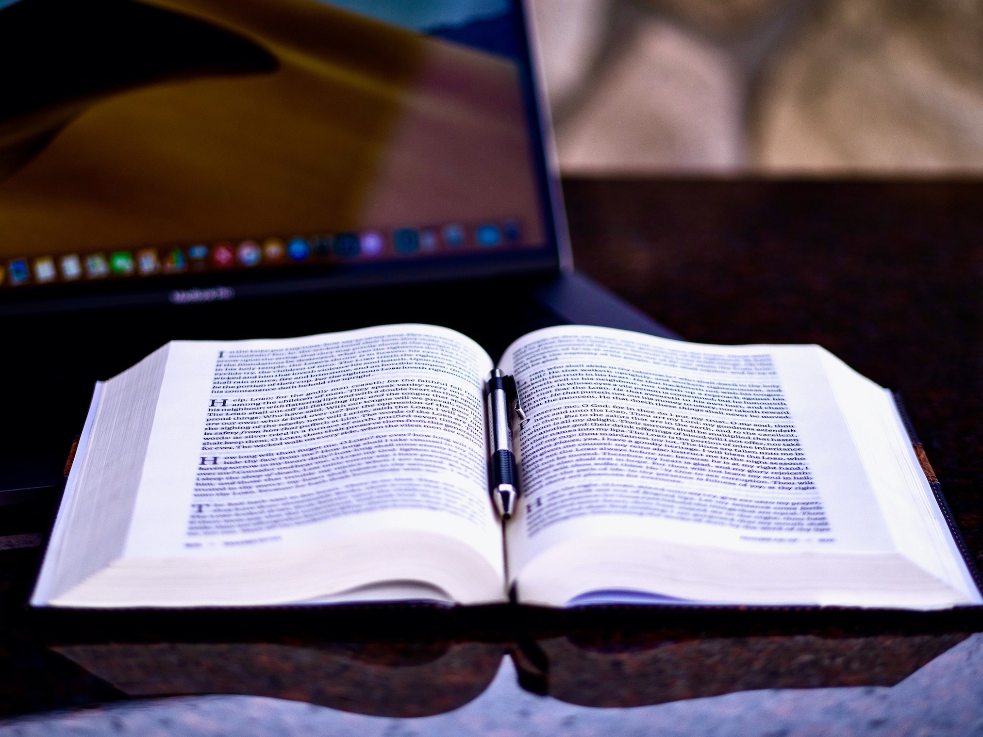 Open Bible in front of laptop computer